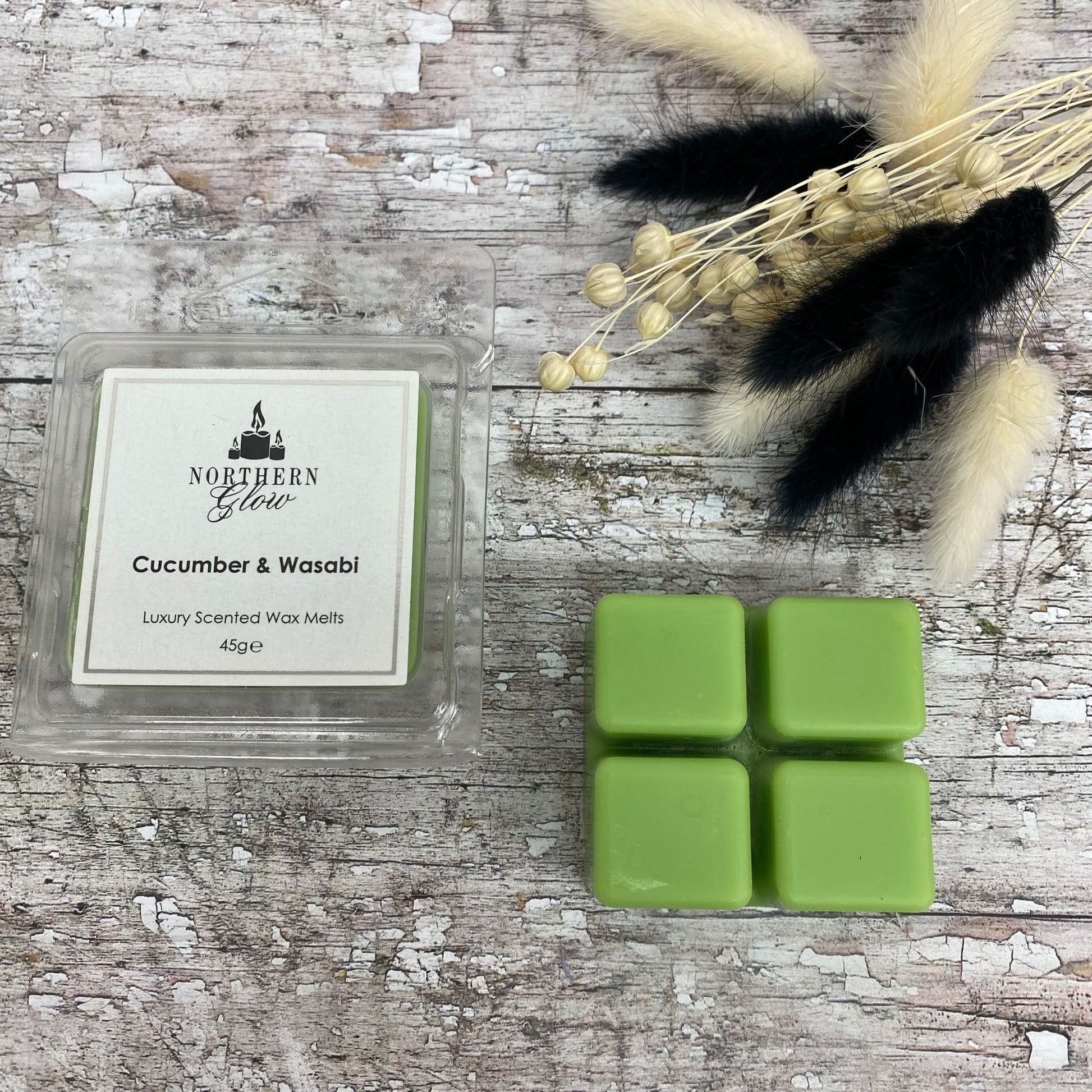 Cucumber and Wasabi Wax Melt is a green colour in a square shape with four breakable cubes in a plastic case. The lablel is white with a silver border and black writing. The logo is at the top with 'Cucumber and Wasabi' in the centre.