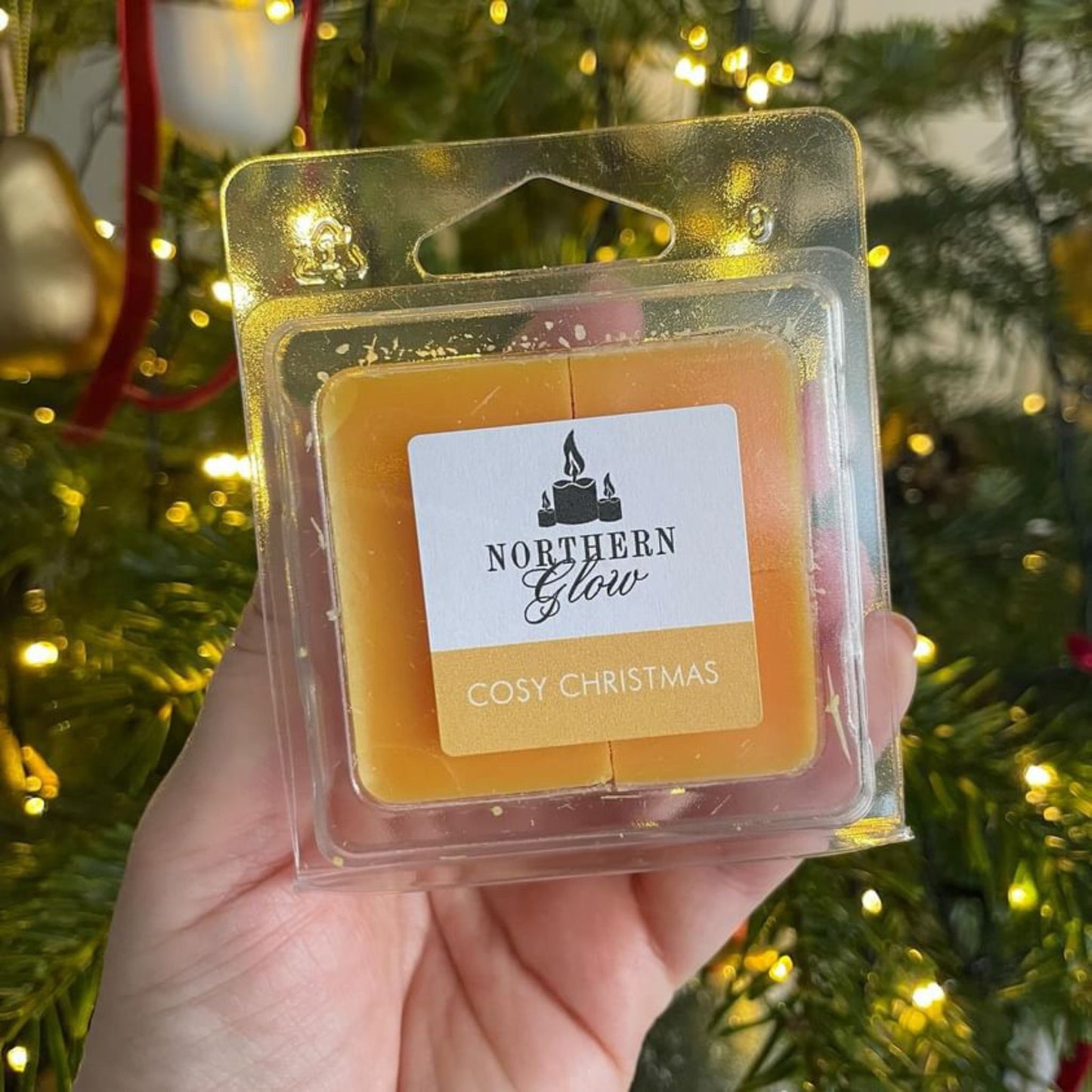 Cosy Christmas wax melt is a yellow colour in a plastic case. The melt has four individual cubes that can be split. The label is white with the logo in the centre. 'Cosy Christmas' is in white writing with a yellow background.