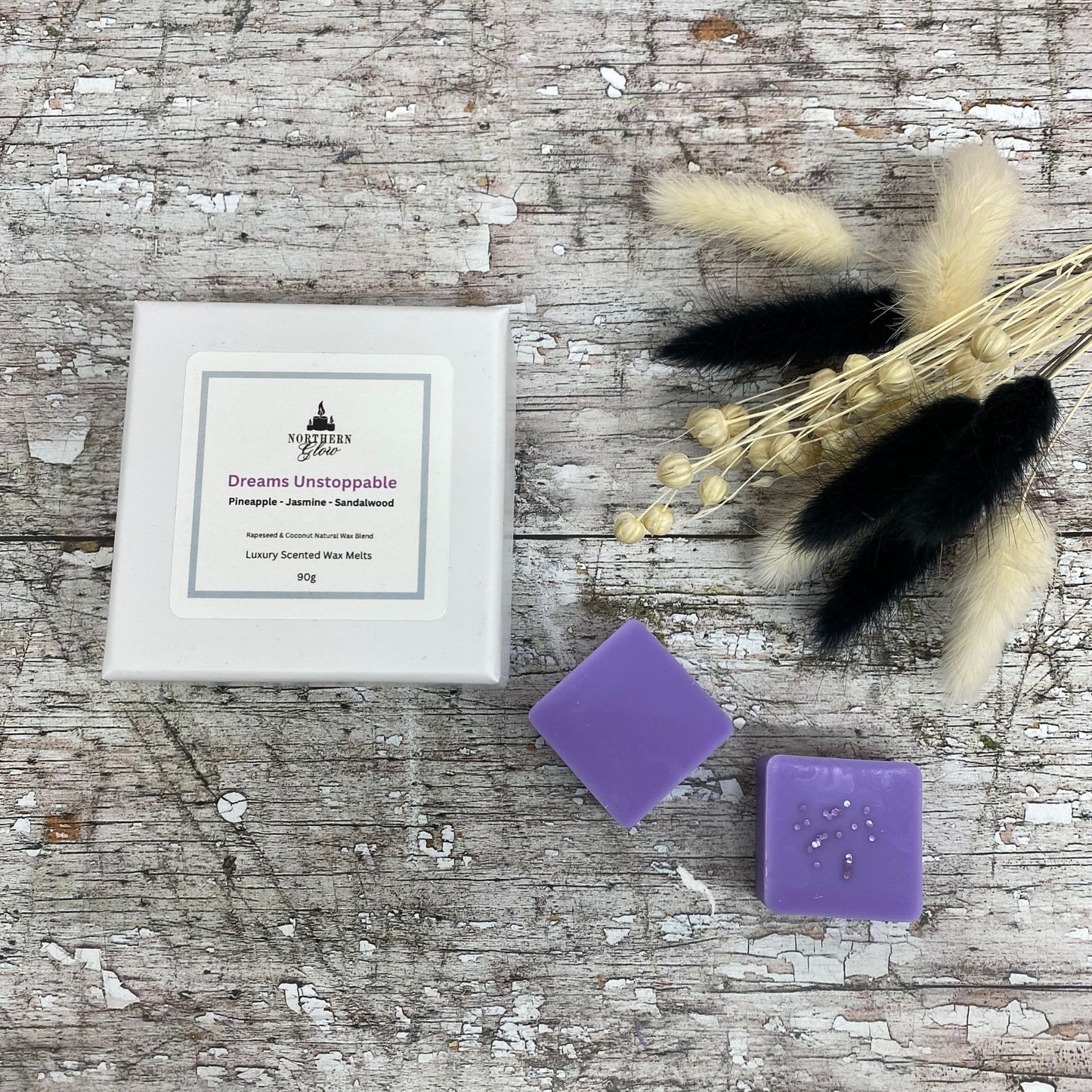 Dreams Unstoppable wax melt is a colour purple and each melt is a square shape in a white, square box. There are eight individual wax melts in the white box. The label is white with a silver border. The logo is at the top with 'Dreams Unstoppable' in purple writing in the centre.