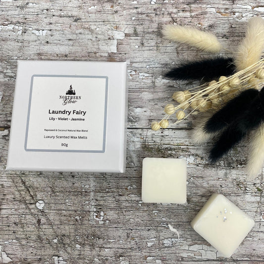 Laundry Fairy wax melt is a white colour and each melt is a square shape in a white box. There are eight individual wax melts in the white box. The label is white with a silver border. The logo is at the top with 'Laundry Fairy' in black writing in the centre.