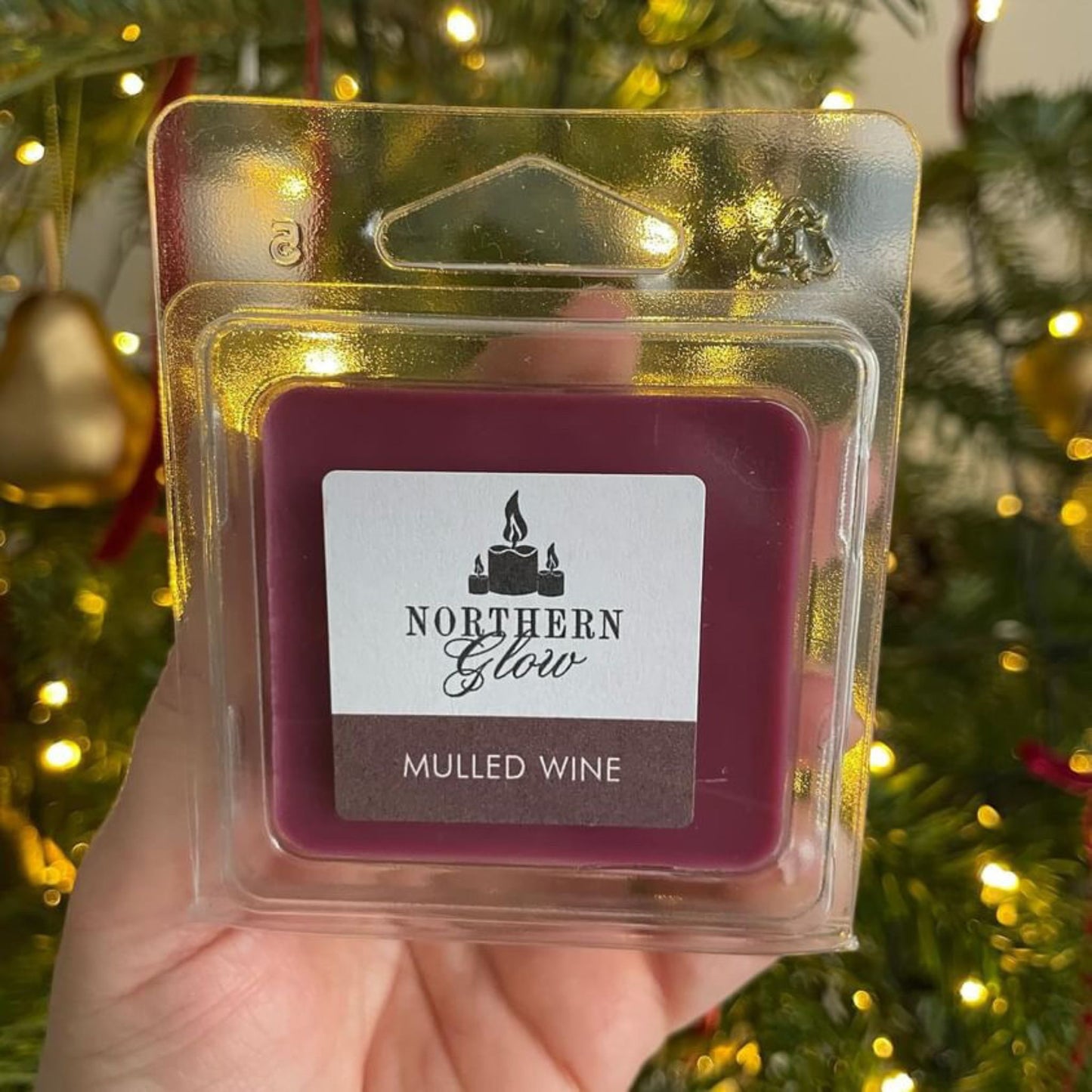 Mulled Wine wax melt is a burgundy colour in a square shape with four individual cubes. It is in a plastic case with a white label on the front with the logo in the centre. 'Mulled Wine' is at the bottom with white writing and a burgundy background.