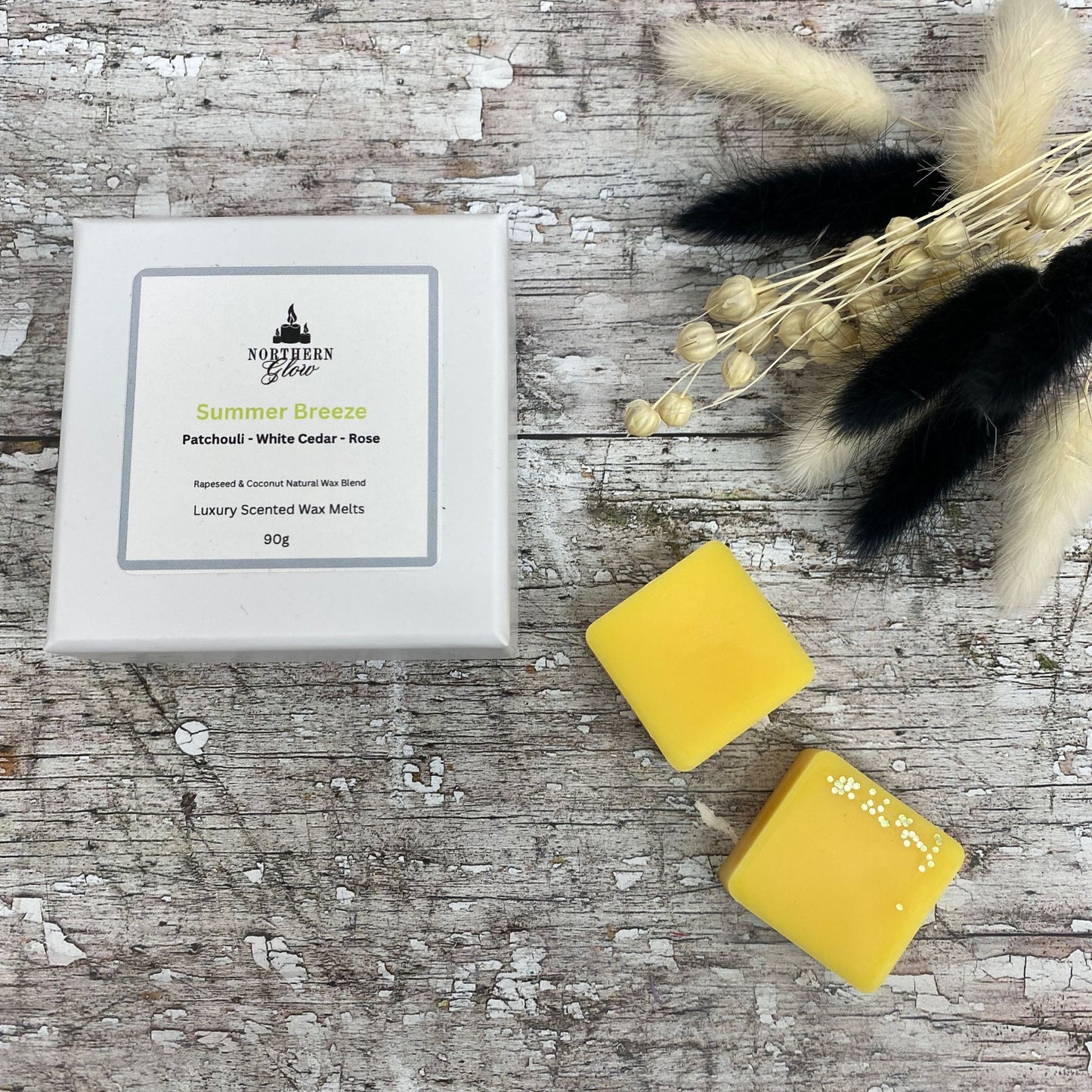 Summer Breeze wax melt is a yellow colour and each melt is a square shape in a white box. There are eight individual wax melts in the white box. The label is white with a silver border. The logo is at the top with 'Summer Breeze' in yellow writing in the centre.