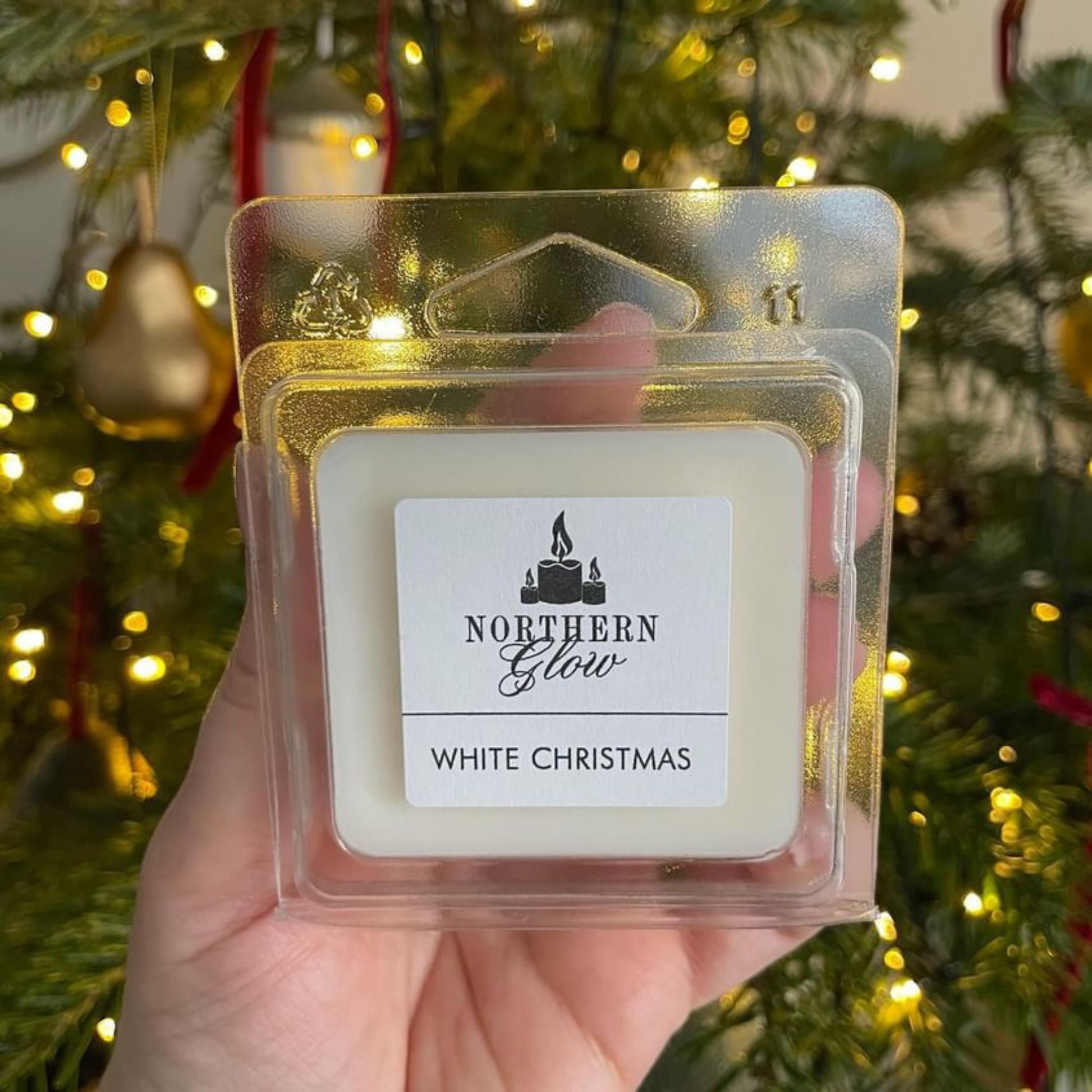 White Christmas wax melt is a white colour and in a plastic case. It is a square shape with four individual cubes. The label is white with the logo in the centre. 'White Christmas' is in black writing.