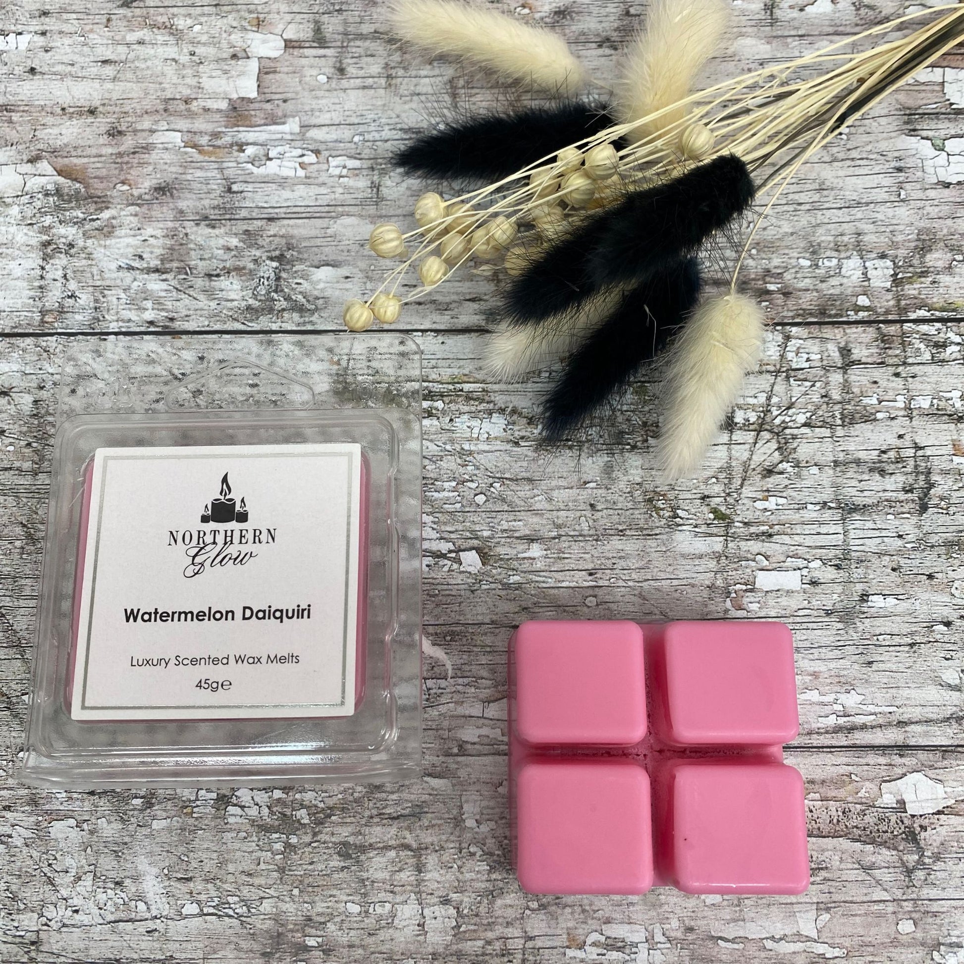 Watermelon Daiquiri Wax Melt is a pink colour and is a square shape with four breakable cubes in a plastic case. The lable is white with a silver border and black writing. The logo is at the top with 'Watermelon Daiquiri' in the centre