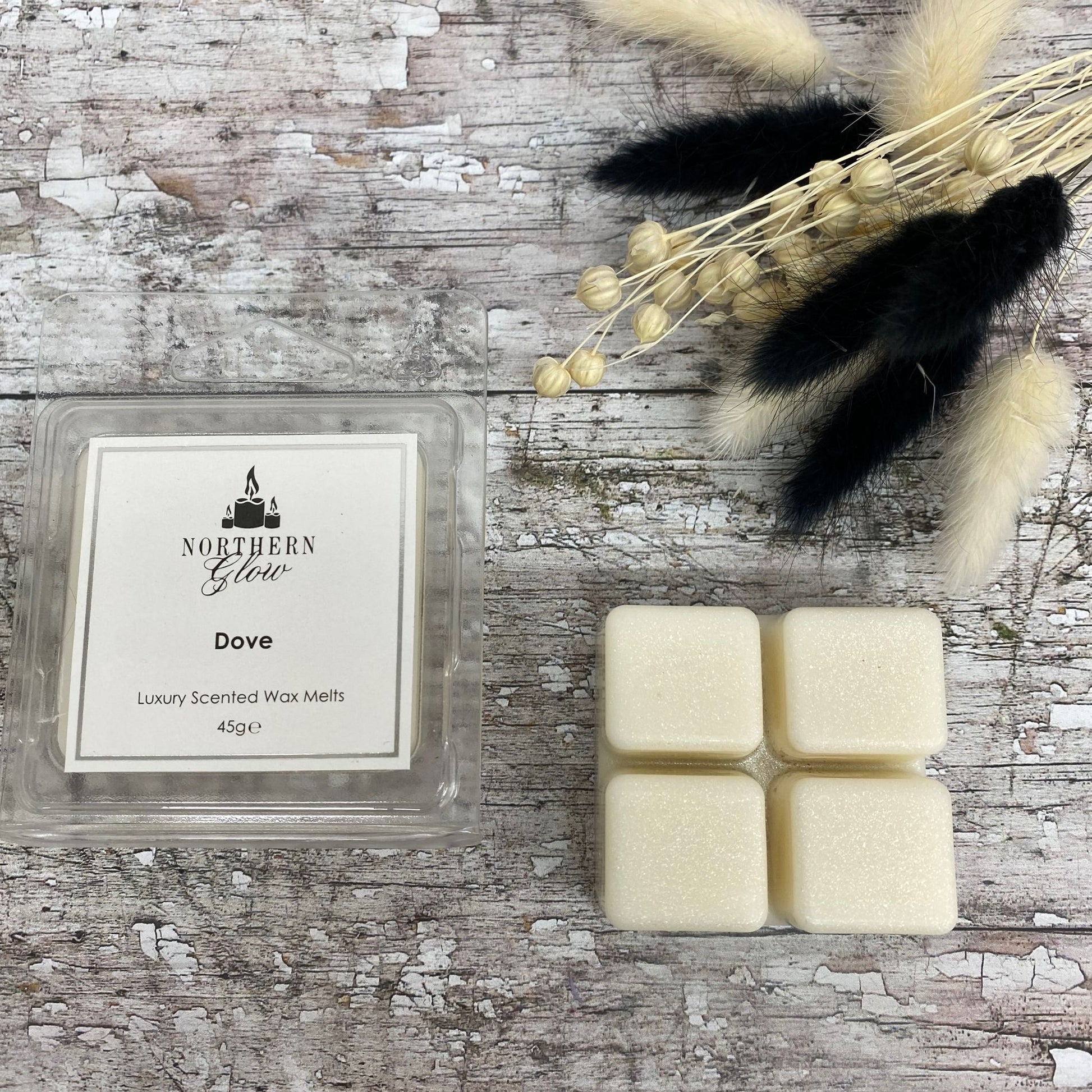 White Dove Wax Melt is a white colour and shaped as a square with four breakable cubes in a plastic case. The lable is white with a silver border and black writing. The logo is at the top with 'Dove' in the centre.